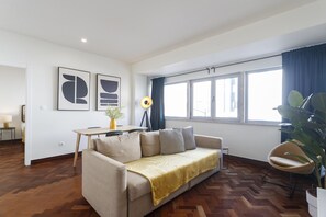 Uma sala de estar moderna com um sofá, uma mesa de jantar e uma janela grande com cortinas.