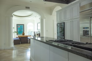 A spacious kitchen with white cabinetry, a large island, and a stainless steel range hood.
