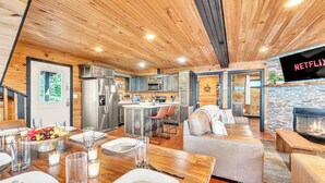 A modern kitchen with a central island, a dining area with a wooden table set for four, and a cozy living area with a fireplace. - Rivers Ledge Cabin with breathtaking views, hot tub, & indoor pool! (Bryant)