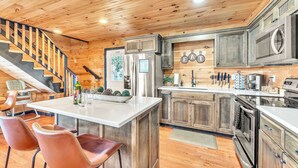 A modern kitchen with wooden cabinets, stainless steel appliances, and a central island with bar stools. - Rivers Ledge Cabin with breathtaking views, hot tub, & indoor pool! (Bryant)