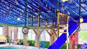 An indoor pool area with a blue slide, rope climbing net, and a stone wall in the background. - Rivers Ledge Cabin with breathtaking views, hot tub, & indoor pool! (Bryant)