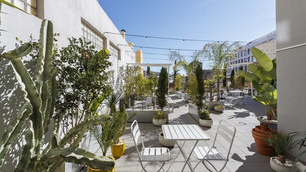 An outdoor patio area with white metal furniture, potted plants, and a clear blue sky.