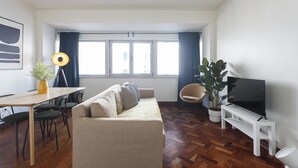 A modern living room with a sofa, a dining table, chairs, a TV, and a potted plant.