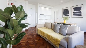 A modern hotel room with a sofa, a dining table, and a kitchen area in the background.