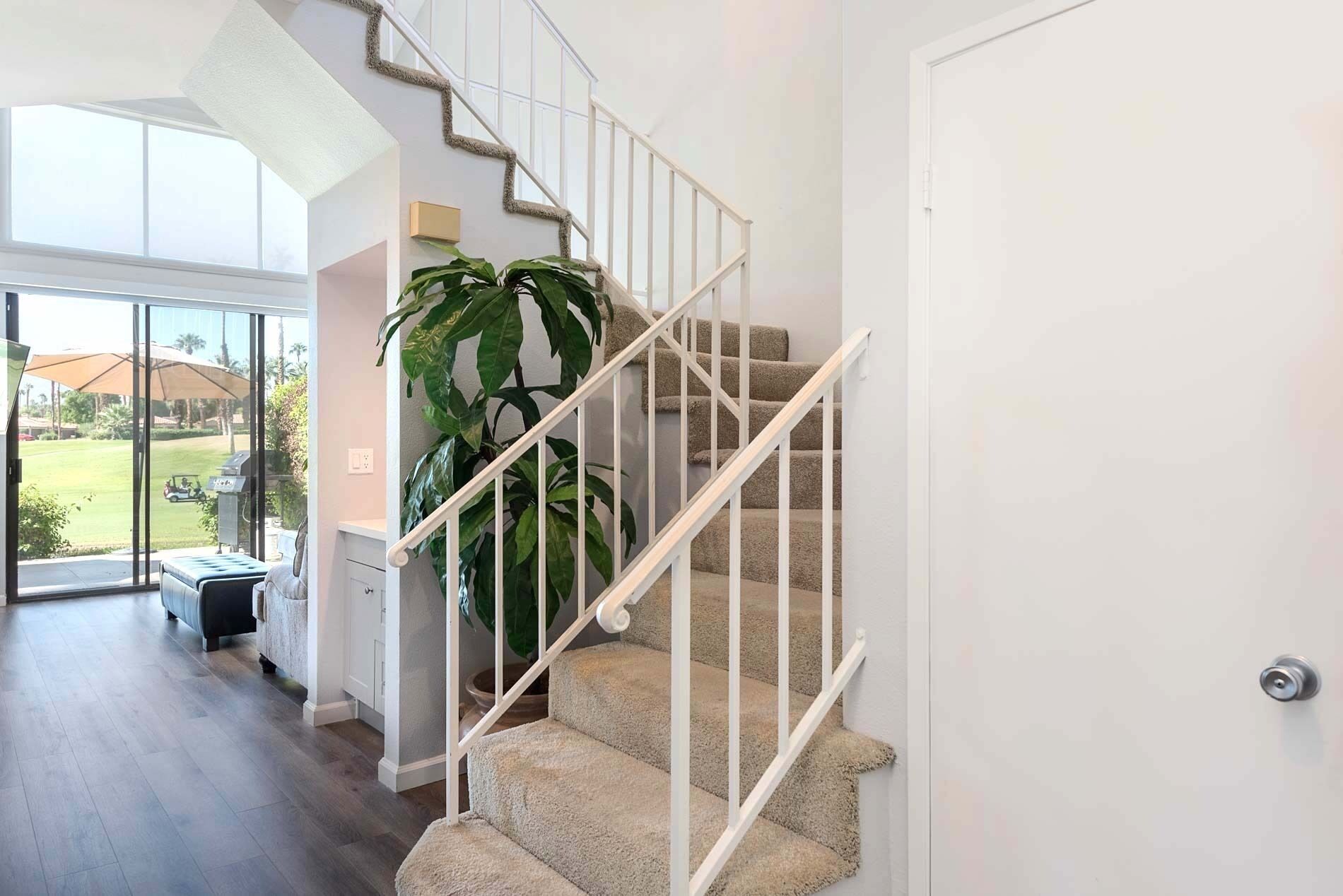 Un escalier dont les marches sont recouvertes de moquette et qui possède des rampes blanches, menant à une pièce dotée d’une grande fenêtre et offrant une vue sur un terrain de golf.