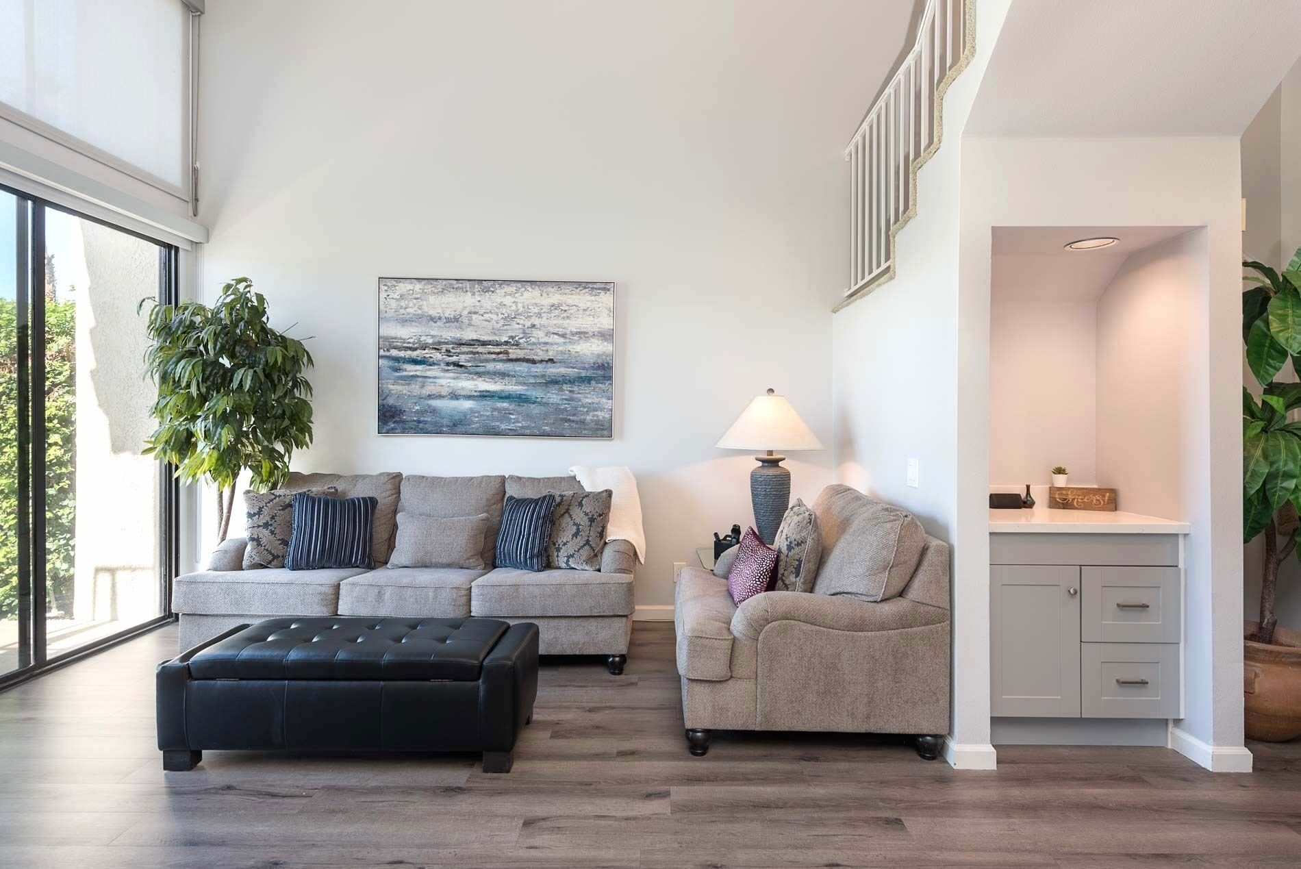 A modern living room with a sofa, ottoman, and a painting on the wall.