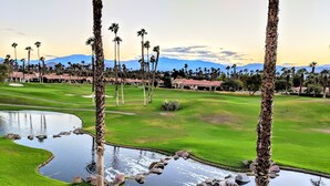 Un parcours de golf avec un étang, des palmiers et des montagnes en arrière-plan.