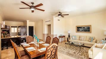 A spacious living area with a dining table set for six, a sofa, a coffee table, and two ceiling fans.