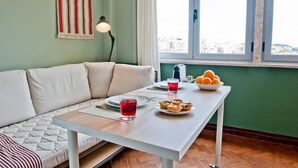 A modern living room with a sofa, a dining table with plates, glasses, and a bowl of fruit.