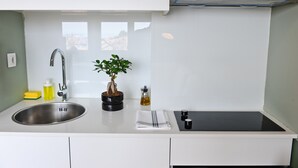 A modern kitchen with a stainless steel sink, a potted plant, and a black induction cooktop.