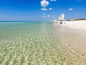 Een strand met helder ondiep water, een zandstrand en een uitgestrekte skyline in de verte.