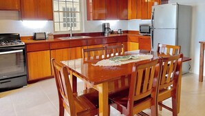 A kitchen with wooden cabinets, a stove, a refrigerator, and a dining table with chairs. - Oceanfront 2 bed/2 bath Velento#4, private dock/beach/pool/free paddle boards (Caye Caulker)