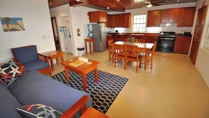 A modern kitchen with wooden cabinets, a dining area with a table and chairs, and a living room with a sofa and coffee table. - Oceanfront 2 bed/2 bath Velento#4, private dock/beach/pool/free paddle boards (Caye Caulker)