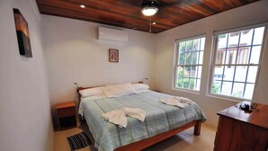 A bedroom with a wooden bed, a bedside table, a desk, and a window with a view of greenery. - Oceanfront 2 bed/2 bath Velento#4, private dock/beach/pool/free paddle boards (Caye Caulker)