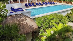 A resort with a swimming pool, lounge chairs, and a thatched-roof hut. - Oceanfront 2 bed/2 bath Velento#4, private dock/beach/pool/free paddle boards (Caye Caulker)
