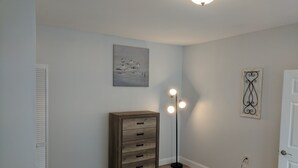 A bedroom with a bed, a dresser, a floor lamp, and artwork on the walls. - DOWNTOWN NEWPORT HOTSPOT! Private Parking included - Open floor plan, spacious! (Newport)