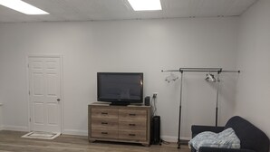 A room with a wooden dresser, a television, a black chair, a clothing rack, and a door. - DOWNTOWN NEWPORT HOTSPOT! Private Parking included - Open floor plan, spacious! (Newport)