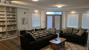 A modern living room with two black sofas, a wooden coffee table, and a patterned rug. There are built-in shelves with decorative items and a large window with blinds. - DOWNTOWN NEWPORT HOTSPOT! Private Parking included - Open floor plan, spacious! (Newport)