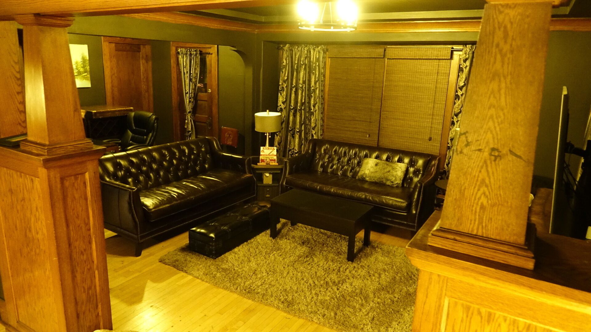 A cozy living room with a dark leather sofa, a matching ottoman, and a wooden coffee table. A lamp and a small table with a book are also visible.