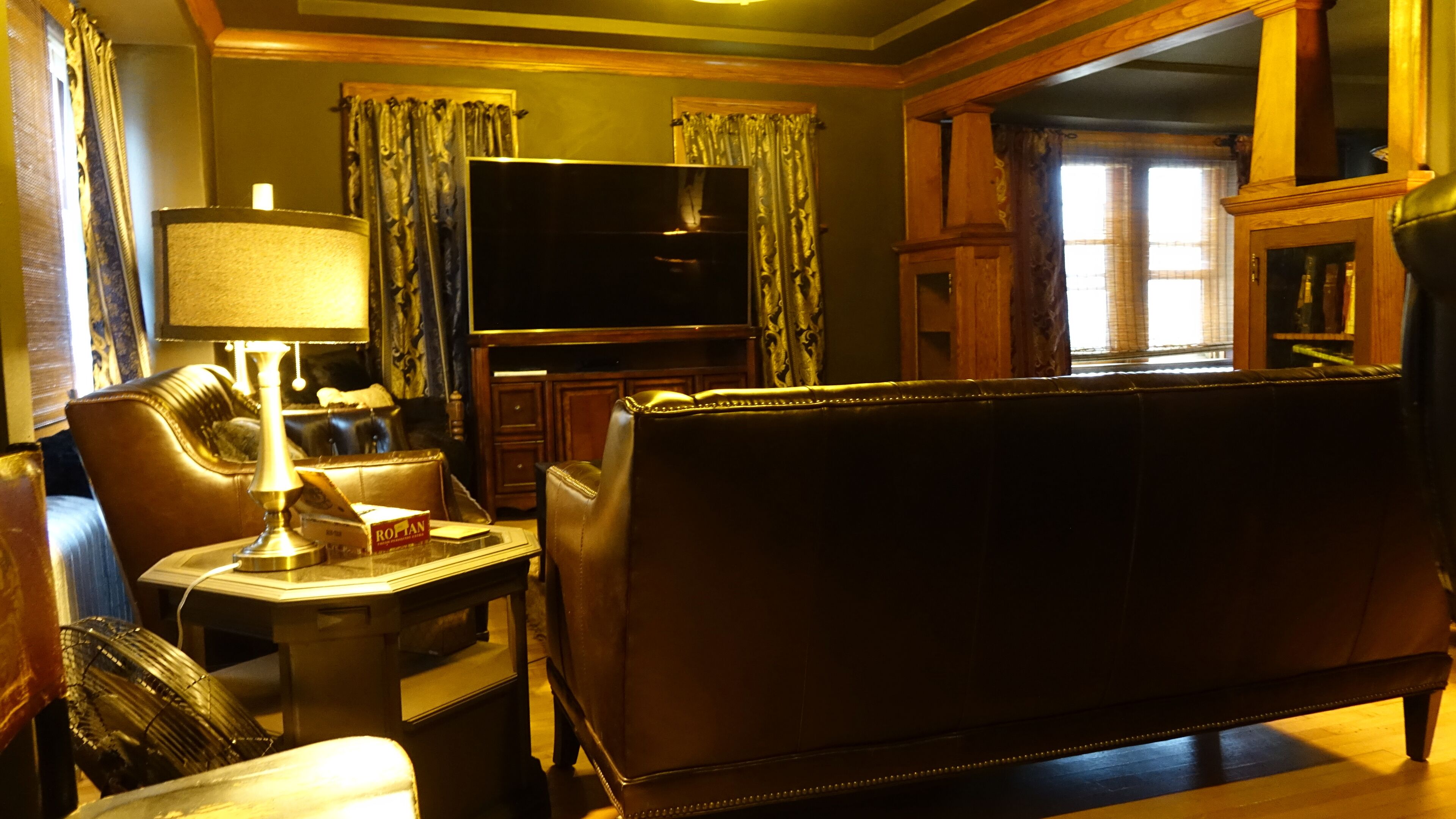 A living room with a leather sofa, a television, a lamp, and curtains.