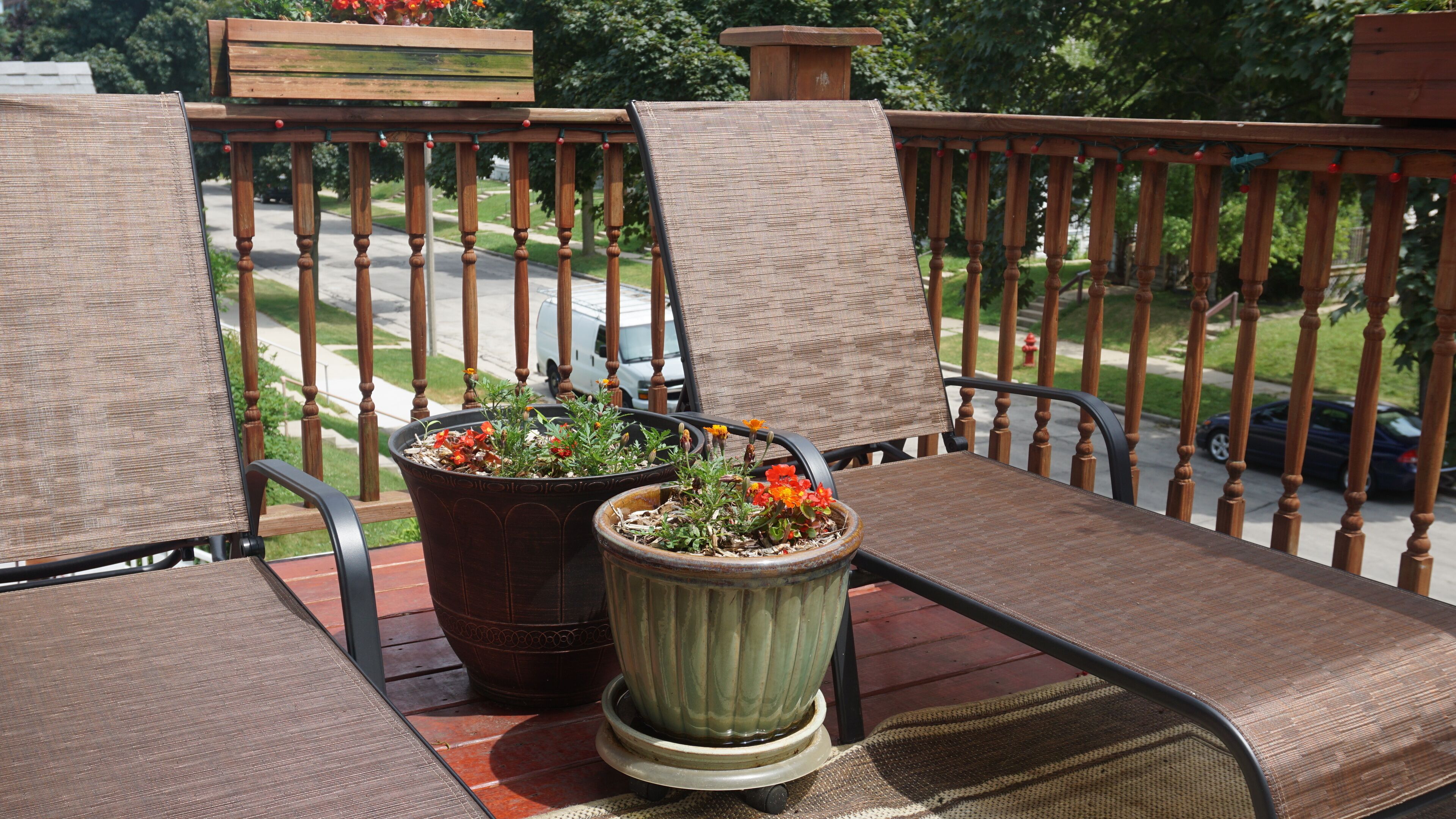 A balcony with two chairs and two potted plants.