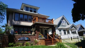 A two-story house with a front porch, a brick foundation, and a wooden staircase leading to the entrance.