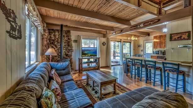 Ein gemütliches Wohnzimmer mit Steinwand, Holzboden und großem Fenster. Es gibt ein Sofa, einen Couchtisch und einen Fernseher.
