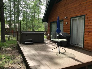 Eine Holzhütte mit einer Terrasse, einem Whirlpool und einem überdachten Grillbereich.