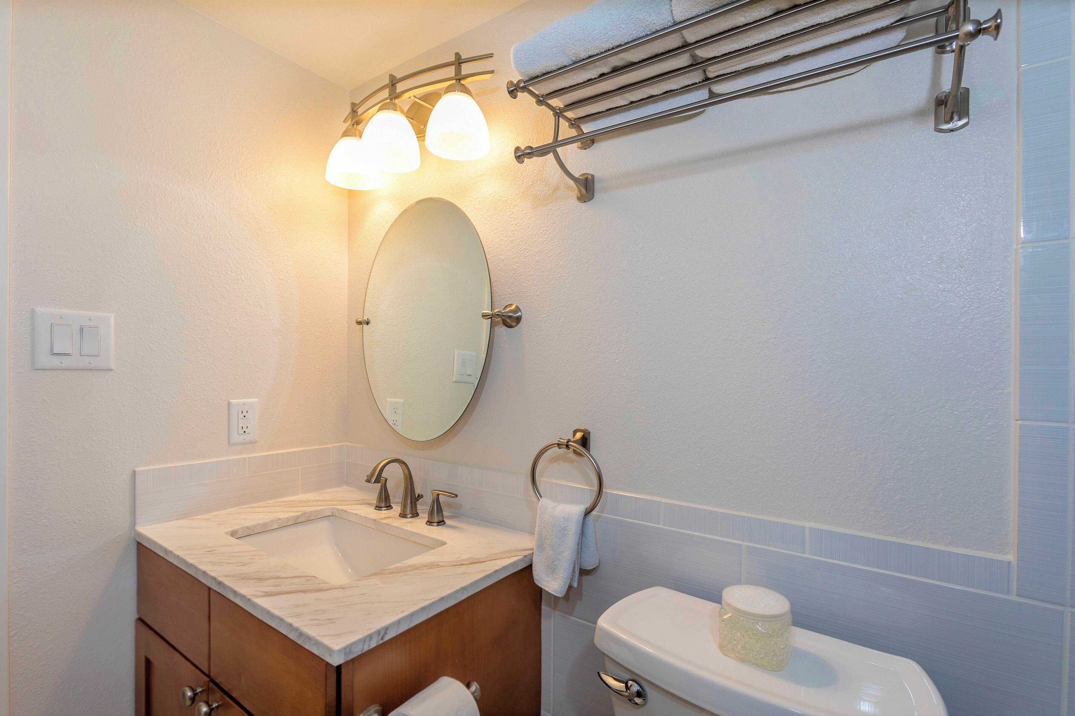 A bathroom with a marble sink, a mirror, a towel rack, and a toilet.