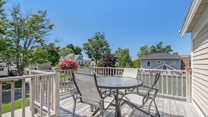A wooden deck with a round table and chairs, surrounded by a white railing.