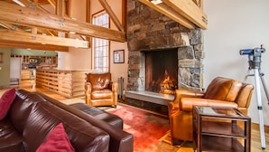 Ein geräumiger Wohnbereich mit Kamin aus Stein, Ledersofas und Holzbalken.
