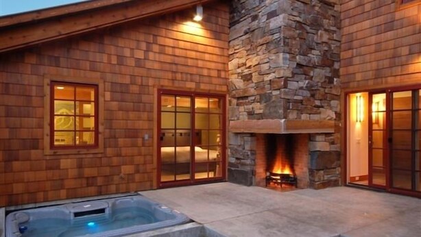 Eine Holzhütte mit Kamin aus Stein, einem Whirlpool und Glastüren, die zum Schlafzimmer führen.