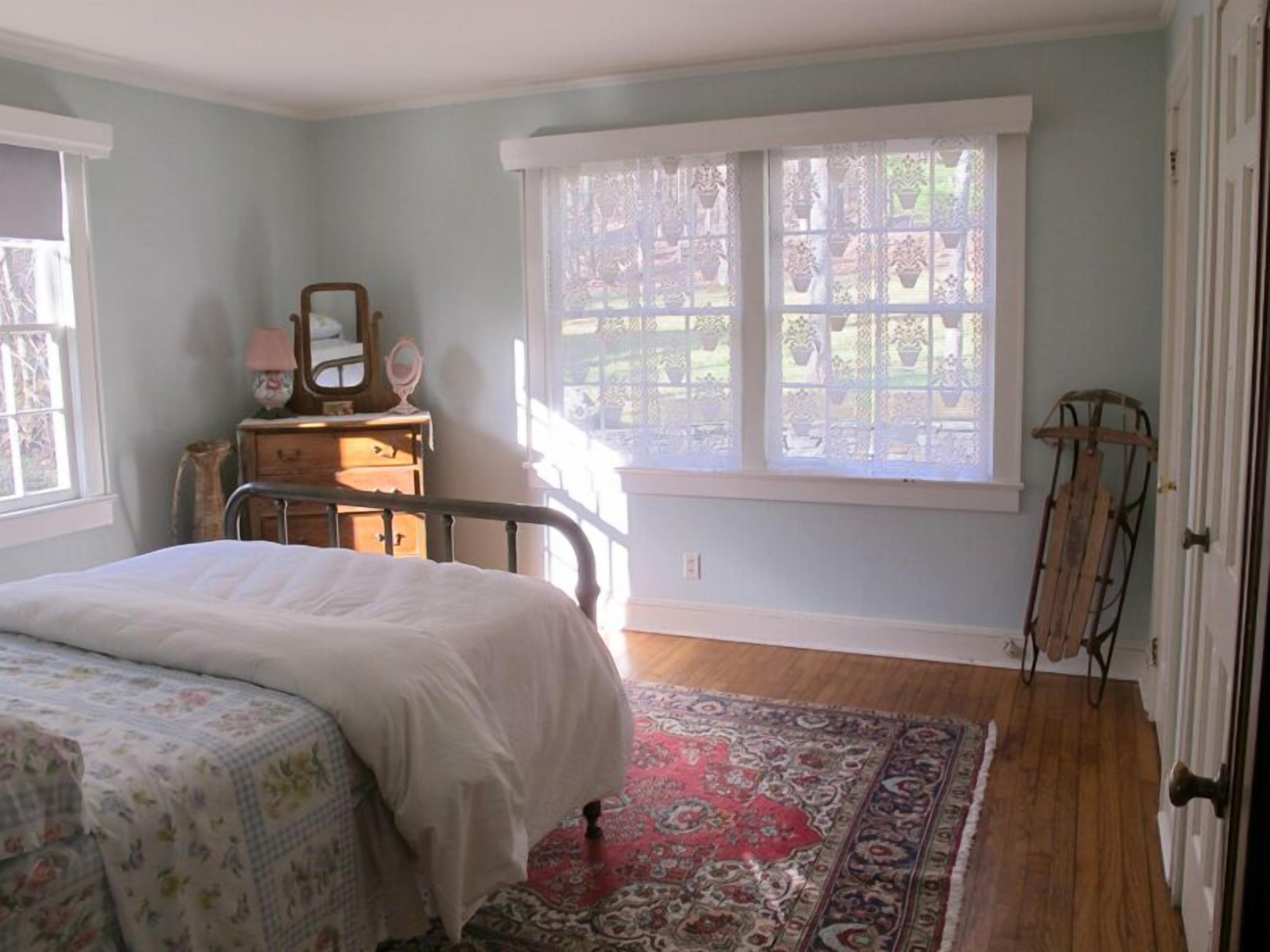 Ein Schlafzimmer mit Bett, Schminktisch, Spiegel und Fenster mit Gartenblick.