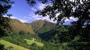 Eine gebirgige Landschaft, mit einem Haus, eingebettet in ein Tal, umgeben von Grün und Bäumen.
