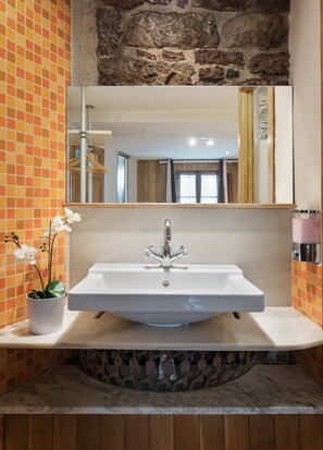 Ein Badezimmer mit einem weißen Waschbecken, einem großen Spiegel und einer Orchidee im Topf.