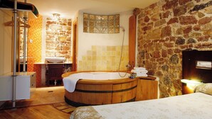 Une salle de bain avec un mur en pierre, une baignoire en bois, un lavabo et une douche.