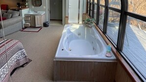 A cozy interior with a large window, a bathtub, a sofa, and a small kitchen area.
