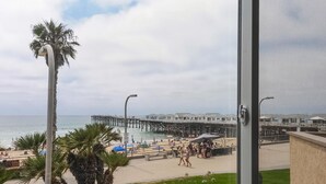 Blick auf einen Strand mit einer Pier, Palmen und Strandstühlen.