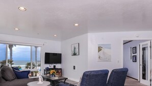 Ein geräumiges Wohnzimmer mit großem Fenster zum Meer, einem wandmontierten Flachbildfernseher und einer gemütlichen Sitzecke mit Couchtisch.