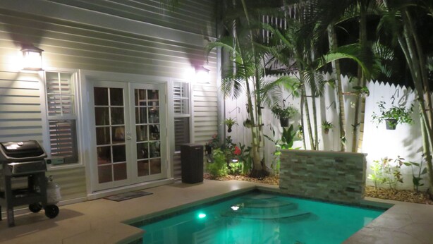 Una piscina con pared de piedra, una parrilla y plantas en macetas.