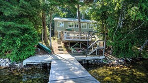 Une cabane avec un quai s’avançant dans un ruisseau aux eaux limpides, entourée d’une forêt dense.