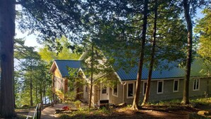 Une cabane rustique avec un toit en métal, entourée de grands arbres et dotée d’une terrasse en bois.