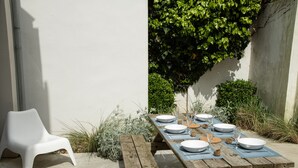 A wooden picnic table set with white plates, glasses, and cutlery, surrounded by greenery and a white wall. - MV 2 - L'Éveil de la Côte - House by the beach (Audresselles)
