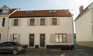 Ein zweigeschossiges Wohnhaus mit Ziegeldach, mehreren Fenstern mit Fensterläden und einem geparkten Auto davor.