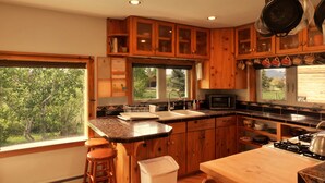A kitchen with wooden cabinets, a sink, a stove, and a window providing a view of greenery outside. - Unique and Spacious Artist's House 5 blocks from Main Street (Driggs)