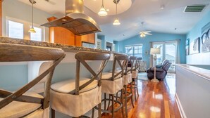 A modern kitchen with wooden bar stools, pendant lighting, and a view to the living area. - ⚓Dock Holiday⚓ Oceanview, Close to Beach🌊 (Carolina Beach)