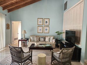 A living room with a sofa, two armchairs, a coffee table, a TV, and framed artwork on the wall.