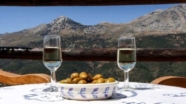 A table with two glasses of wine and a bowl of olives, set against a mountain backdrop.