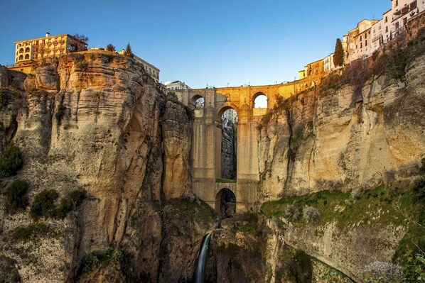A historic stone bridge with arches, a waterfall, and buildings on the cliffs.