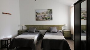 A bedroom with two beds, a ceiling fan, a painting on the wall, and a wooden floor.